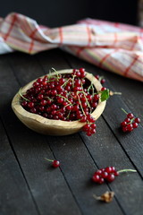 red currant in wooden plate on dark wooden background.