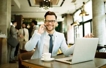 Obraz premium Young businessman uses a laptop in a cafe and talking mobile