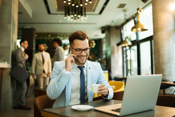 Fototapeta premium Young businessman uses a laptop in a cafe and talking mobile