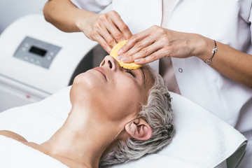 Beautiful senior woman having chemical peeling beauty treatment. The expert beautician is applying...