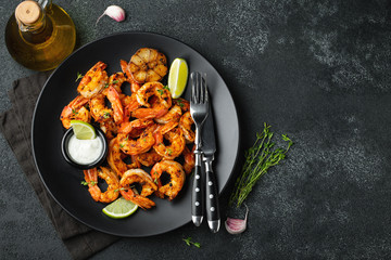Grilled shrimps or prawns served with lime, garlic and white sauce on a dark concrete background. Seafood. Top view with copy space. Flat lay - obrazy, fototapety, plakaty