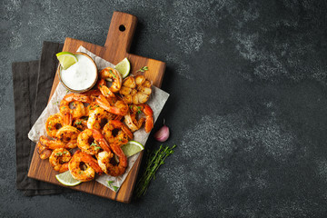 Grilled shrimps or prawns served with lime, garlic and white sauce on a dark concrete background....