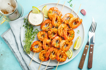Grilled shrimp skewers or langoustines served with lime, garlic and sauce on a light blue concrete...
