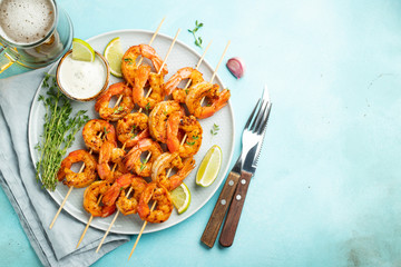 Grilled shrimp skewers or langoustines served with lime, garlic and sauce on a light blue concrete background. Seafood and beer. Top view with copy space. Flat lay