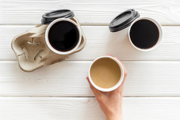 paper cups with black coffee and cappuccino in hand cappuccino to take away on white wooden background top view