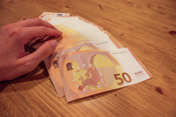 Female woman hand holding many 50 euro banknotes on a wooden table