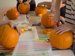 Group of people carving pumpkin to make Jack-o-lantern. Creating traditional decoration for Halloween and Thanksgiving. Cutted orange pumpkin lay on table.