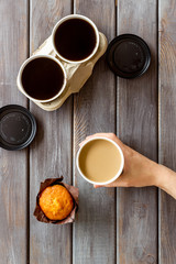 Coffee to take away in paper cups in hand with muffin on wooden table background top view