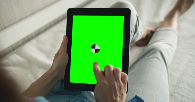 Female lying in tablet and holding greenscreen tablet, making pick-up gesture, touching screen