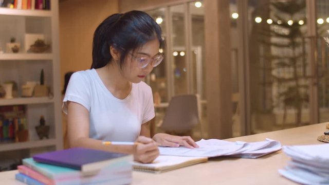 Asian student women reading books in library at university. Young undergraduate girl do homework, read textbook, study hard for knowledge on lecture desk at college campus overtime night. Slow motion.