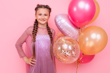 Fototapeta na wymiar Happy and beautiful teen girl holding a bunch of colorful balloons and looking at camera with smile on pink background
