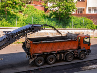 Milling machine removes old asphalt from the road and transports it to a truck.