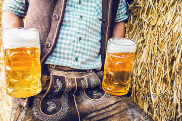 Mann in bayerischen lederhosen mit zwei bierkrügen