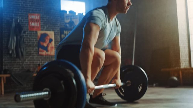Handsome Muscular Man Does Overhead Deadlift with a Barbell in a Small Authentic Gym. Athletic Man Training His Arm Muscles and Exercises with Barbell. Workout in the Hardcore Gym. Warm Light.
