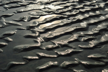 Abstract shop of rippled sand surrounded by pools of seawater reflect the sun.