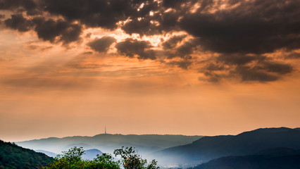 Naklejka premium Dark morning clouds with sun rays and mist in the valley - on the horizon is the outline of the radio tower