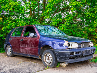 An abandoned car wreck with broken windows in the edge of parking lot
