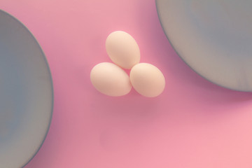 A light blue neutral plate with white chicken eggs on a neutral pink background. Free space to write.