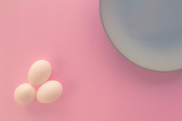 A light blue neutral plate with white chicken eggs on a neutral pink background. Free space to write.