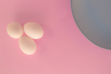 A light blue neutral plate with white chicken eggs on a neutral pink background. Free space to write.