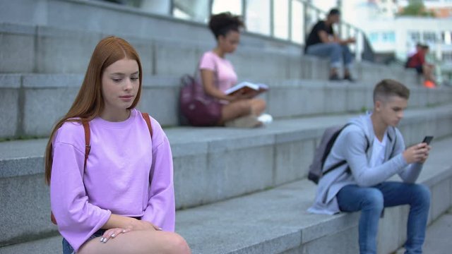 Unhappy teen female suffering from unrequited love looking at male classmate