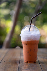 Ice tea with milk in plastic glass on wooden table.