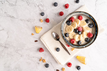 Fresh milk oatmeal with sliced blueberries and raspberries in a bowl on the white marble floor.