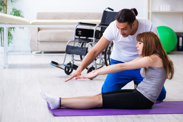 Male physiotherapist doing exercises with injured woman on floor