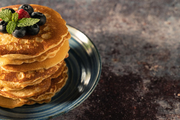 Close up delicious pancake with blueberries, raspberries in blue dish on rust table.