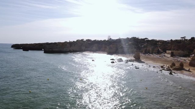 Sea cliffs strech out from Albufeira beach silhetted by sun, Portugal, wide.