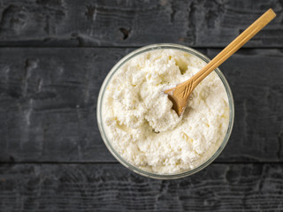 Wooden spoon in a jar with fresh cottage cheese on a rustic table. The view from the top.