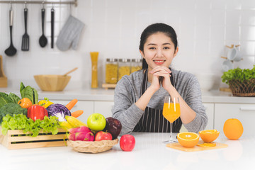 Portrait of beautiful asian woman, housewife with orange juice in white kitchen with plenty of...