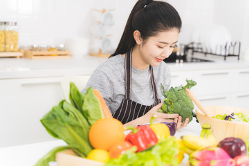 Beautiful asian woman is preparing to cook healthy food which consists of a variety of fruits and vegetables for the family. Housewife is smiling and holding broccoli.