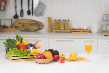 One glass of orange juice and a slice of orange with many vegetables and fruits on a white table in the kitchen