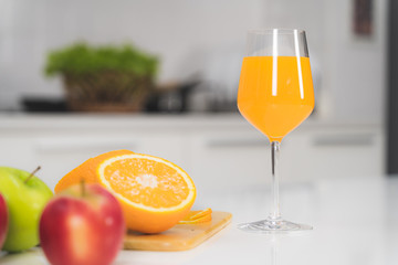 One glass of orange juice and a slice of orange on a white table in the kitchen