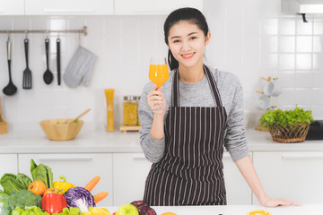 Portrait of beautiful asian woman, housewife with orange juice in white kitchen with plenty of...