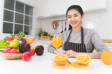 Portrait of beautiful asian woman, housewife with orange juice in white kitchen with plenty of...