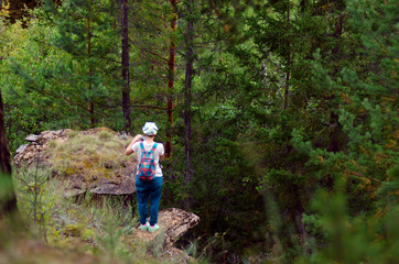 Naklejka na ściany i meble Yakut Asian girl tourist with a backpack takes pictures on the phone view opens to the hat of the erosion shape of the relief of the fungus in the wild taiga in Tianka.