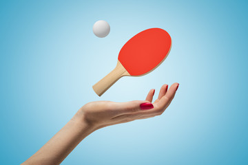Female hand with ping pong racket and ball above on blue background
