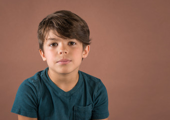 Handsome serious school age boy in teal t shirt looking at camera isolated on brown background - 284969270