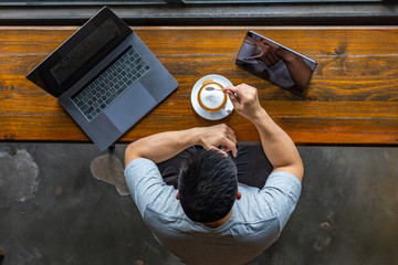 Asian freelancer enjoying coffee with laptop and tablet on table