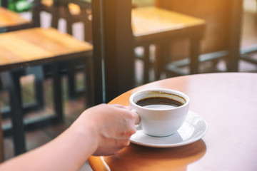 Closeup image of a hand holding a cup of hot coffee on table