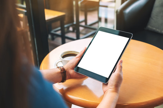 Mockup image of hands holding black tablet pc with blank white screen with coffee cup on wooden table
