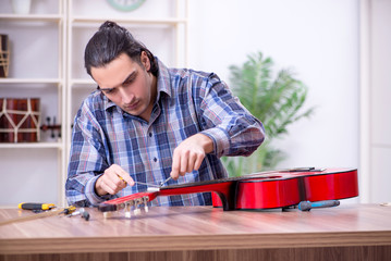 Young handsome repairman repairing guitar