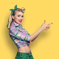 Photo of woman, dressed in pinup style, showing something or copyspace, over orange-yellow background, square composition