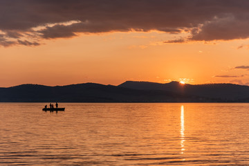 Burning red sunset on the river. Men riding boat. Silhouette of mountains on the background. Beautiful clouds in the sky.