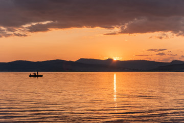 Obraz premium Burning red sunset on the river. Men riding boat. Silhouette of mountains on the background. Beautiful clouds in the sky.