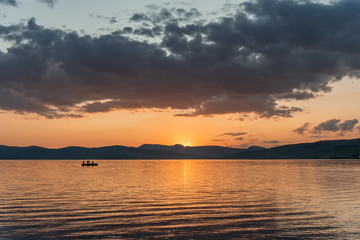 Obraz premium Burning red sunset on the river. Men riding boat. Silhouette of mountains on the background. Beautiful clouds in the sky.
