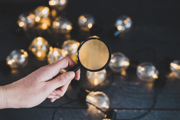 hand holding magnifying glass analyzing different ideas in shape of lightbulb string lights