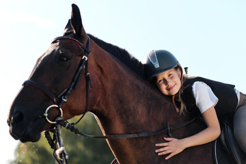 Girl teenager jockey sits on a brown horse, hugs and strokes her.